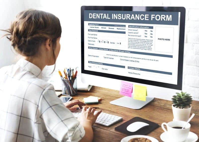 Woman filling out a dental insurance for Levine Orthodontics, an orthodontist in Cape Coral and Fort Myers, FL form on a computer screen in a modern office setting, with office supplies and a plant on the desk