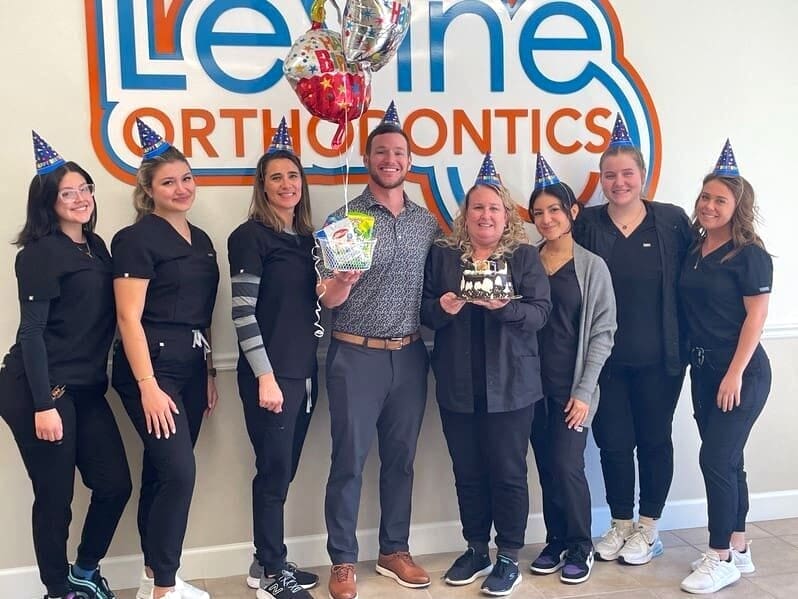Levine orthodontics team standing in front of logo wall of an orthodontist in Fort Myers, FL.